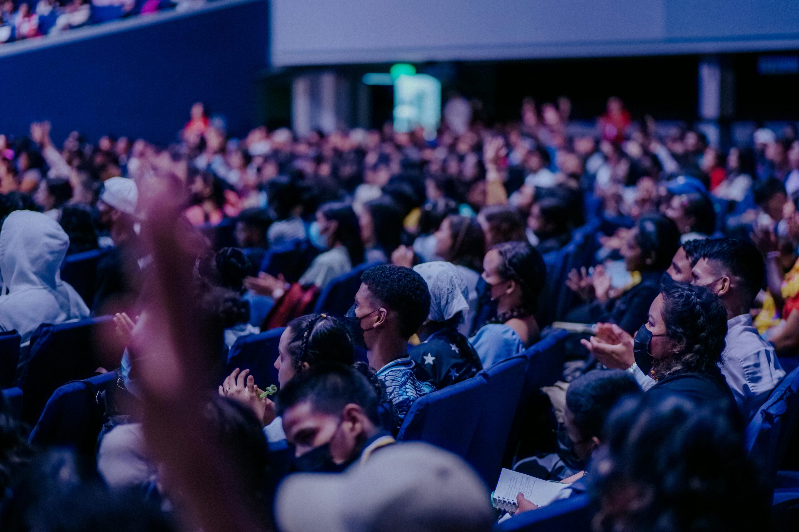 A large, diverse audience attentively watching a live event indoors, seated in rows.